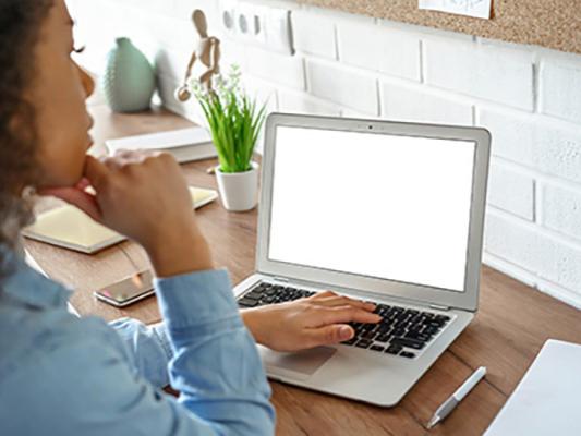 A female student wearing a blue shirt is pictured working at a laptop.