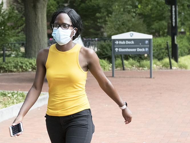 A student in a yellow shirt walks along Pollock Road wearing a mask