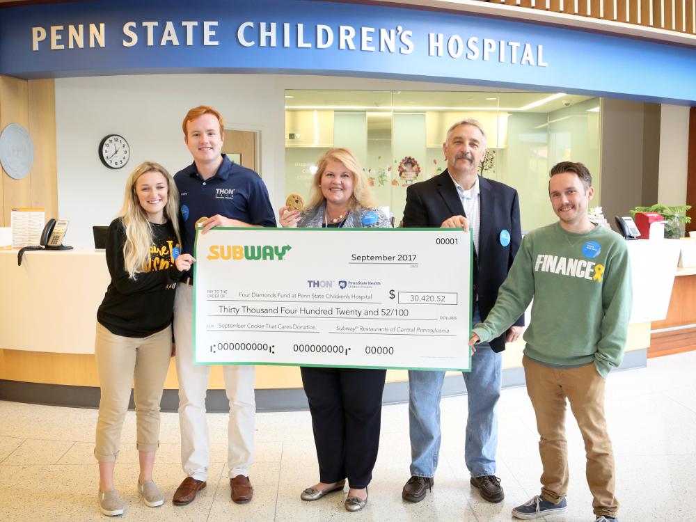 Five people pose for a photo while holding an oversized check in the amount of $30,420.52, from Subway to “Four Diamonds at Penn State Children’s Hospital.”
