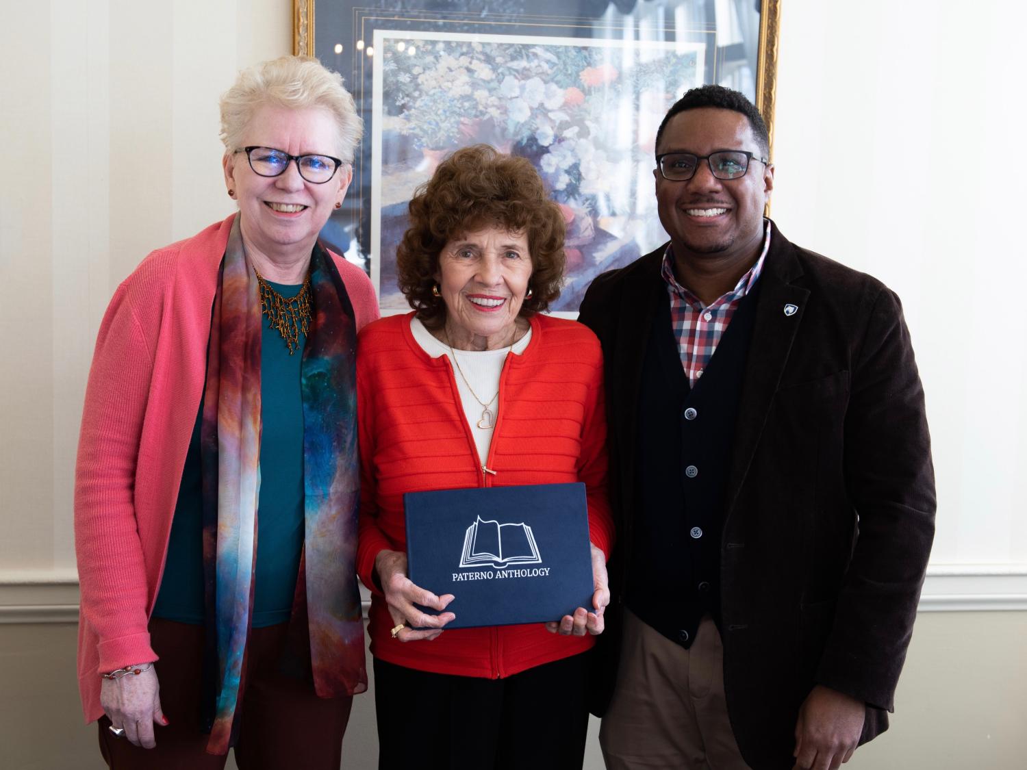 woman holding blue book in center, standing with man and second woman