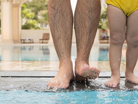 Legs of a parent and child walking into a pool.