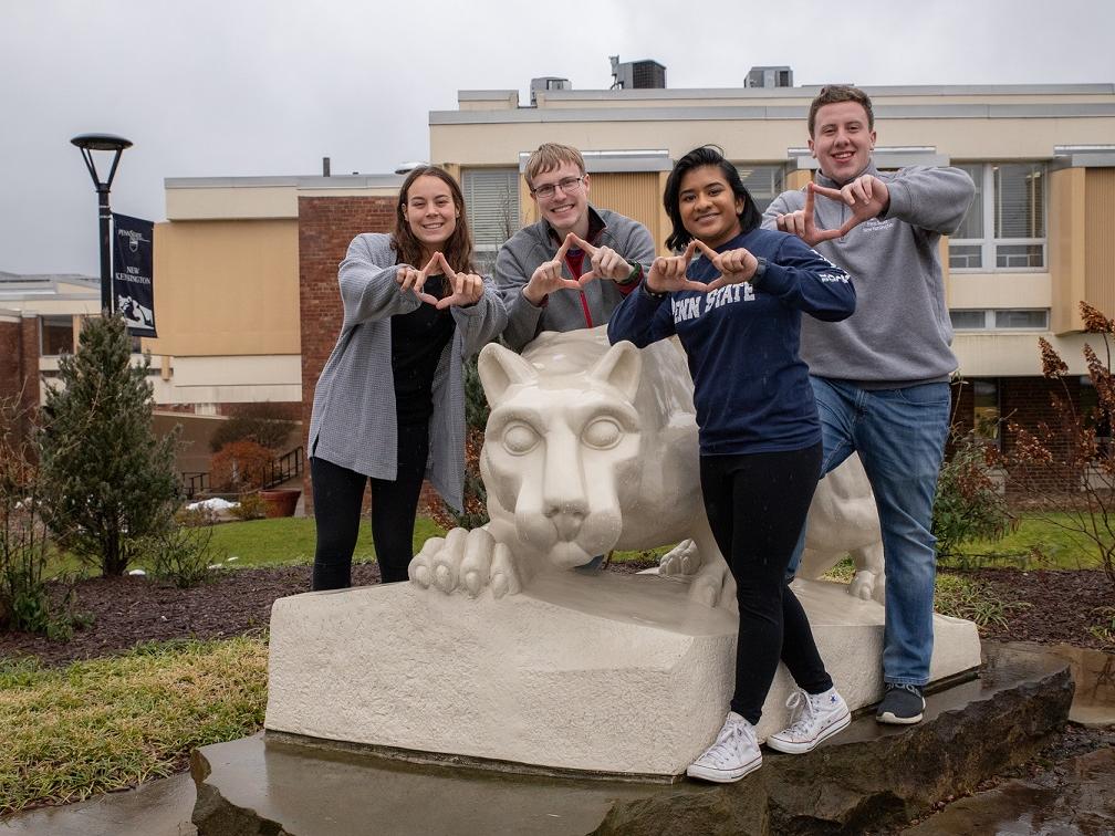 Four students stand by lion statue