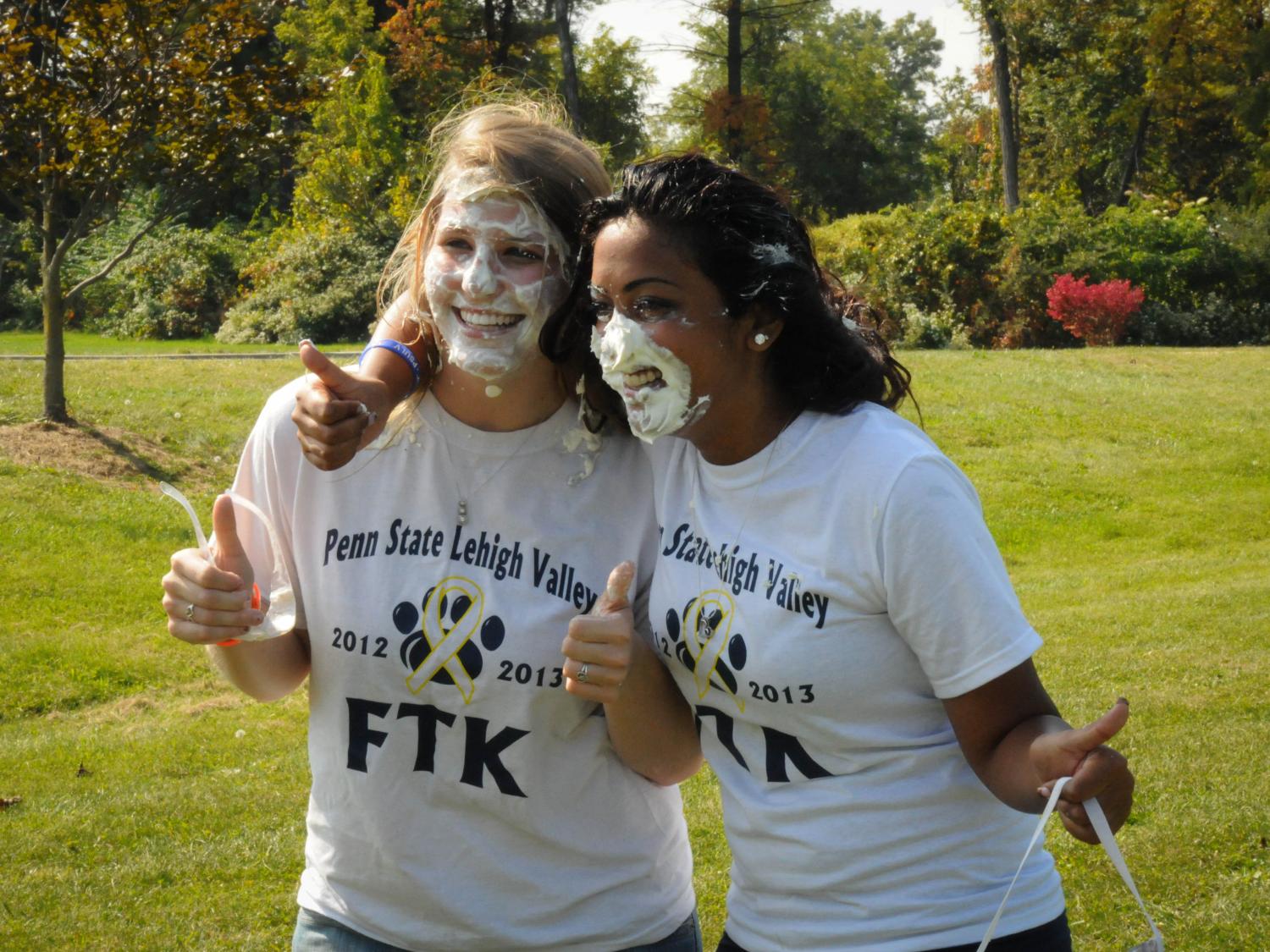 Two students smile for camera after having pies thrown in the faces.