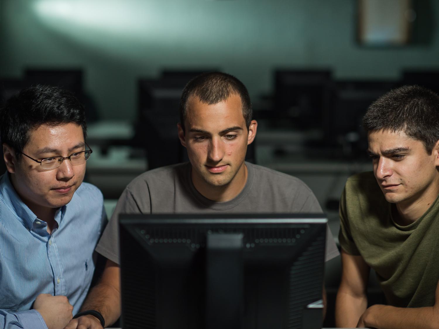 A professor and two students work on a computer.