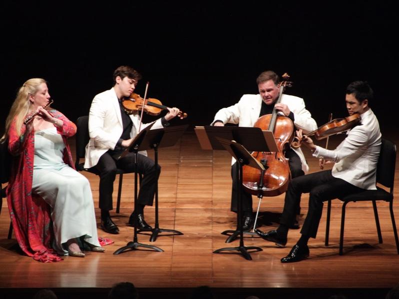 Four musicians sit in a semi circle on stage and perform.