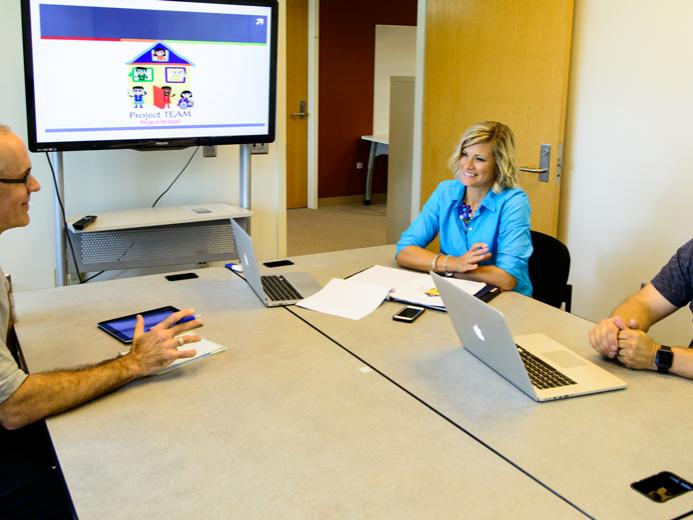 Three members of Project TEAM talk around a table.