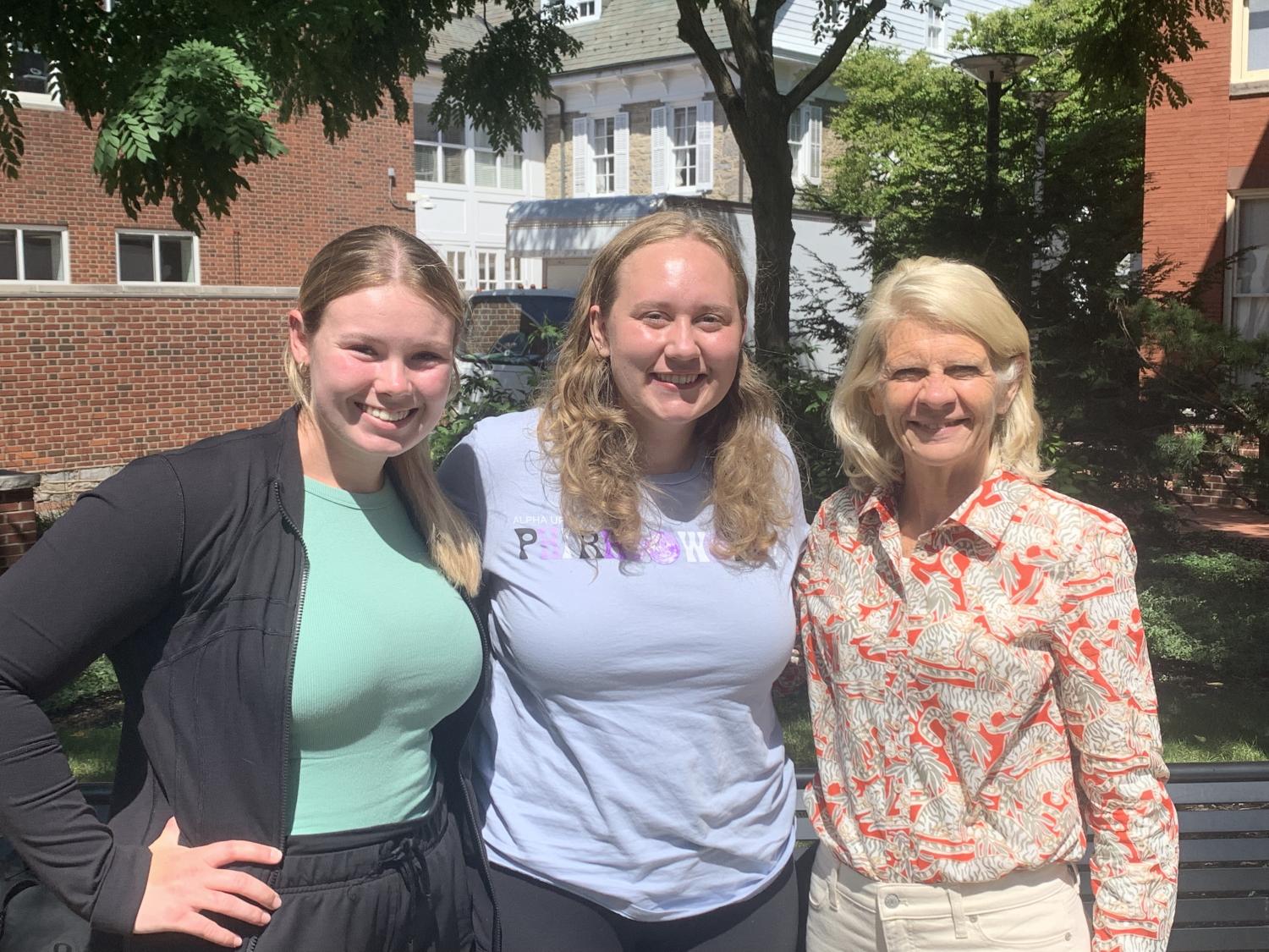 Two undergraduate students pose with a professor in a courtyard smiling. 
