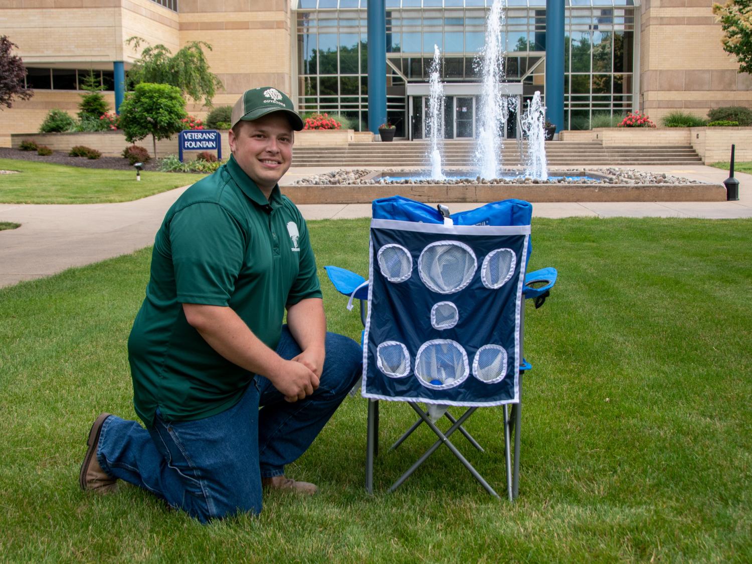 Student Trey White kneels in the grass next to the Chillin' Chair