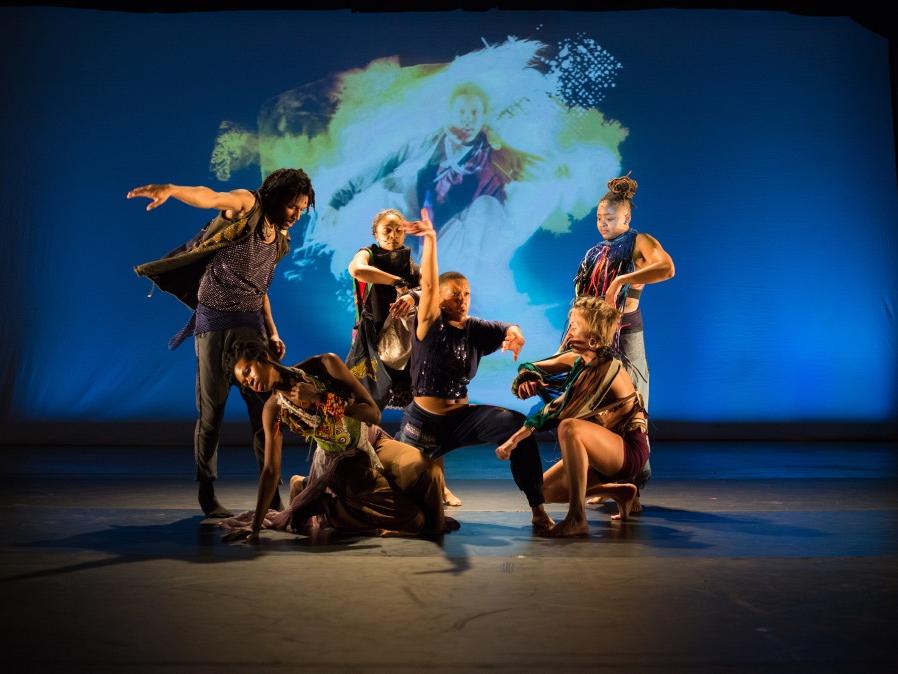A group of people arranged in a cluster make gestures and pose.
