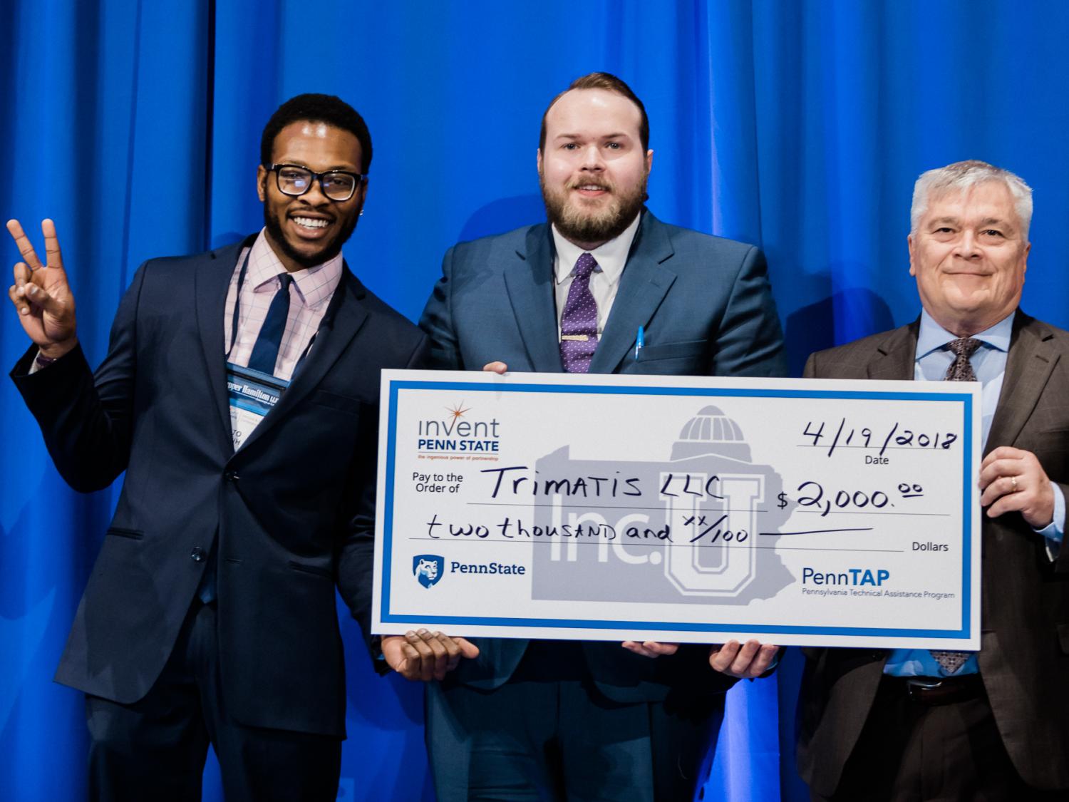 Penn State President Eric Barron, right, awards $2,000 at the 2018 Invent Penn State Venture & IP Conference to Trimatis' Tito Orjih, left, and Jason Lehrer.