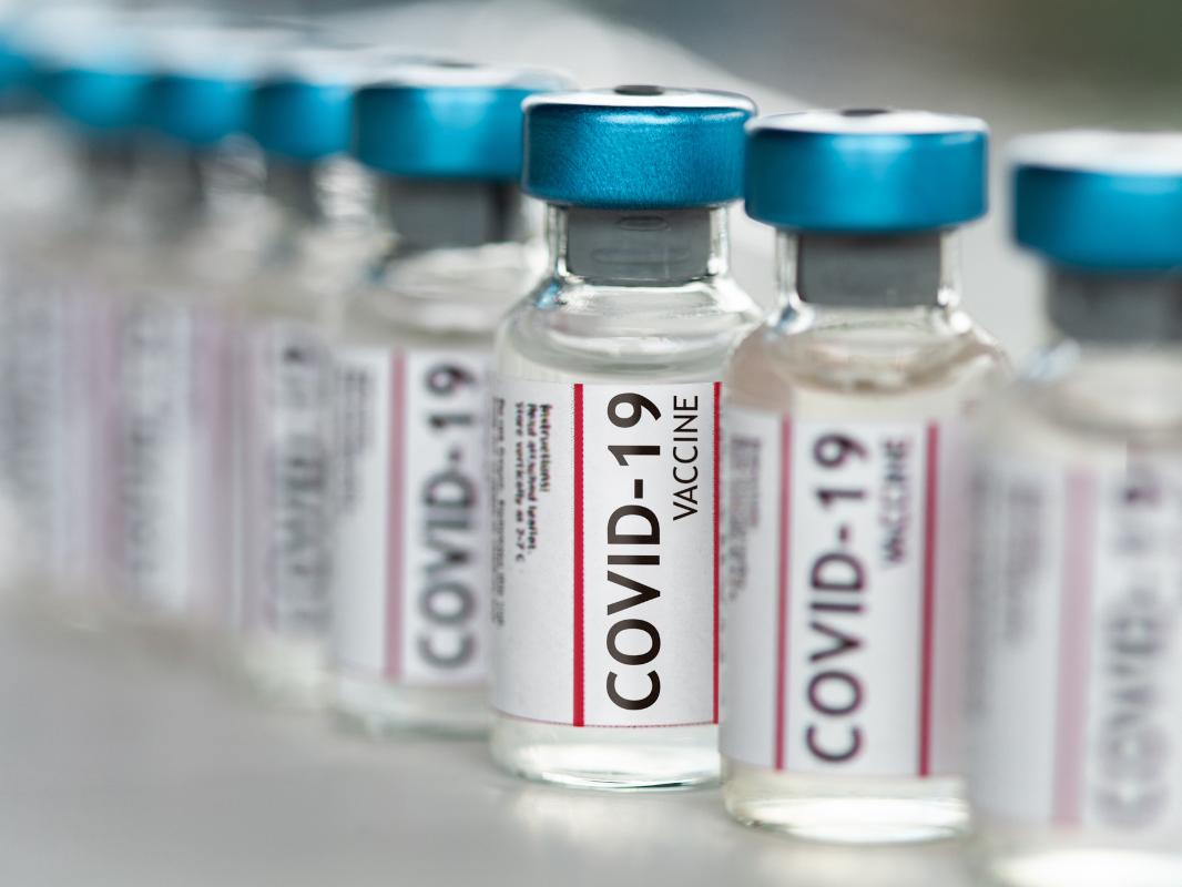 Several small bottles labeled “COVID-19 vaccine” are side-by-side on a table.