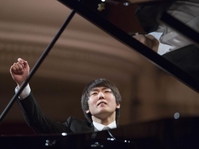 Seong-Jin Cho sits at a piano with his right armin midair.