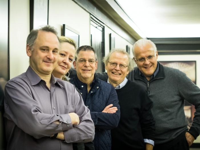 The musicians of Windscape stand shoulder to shoulder against a wall.