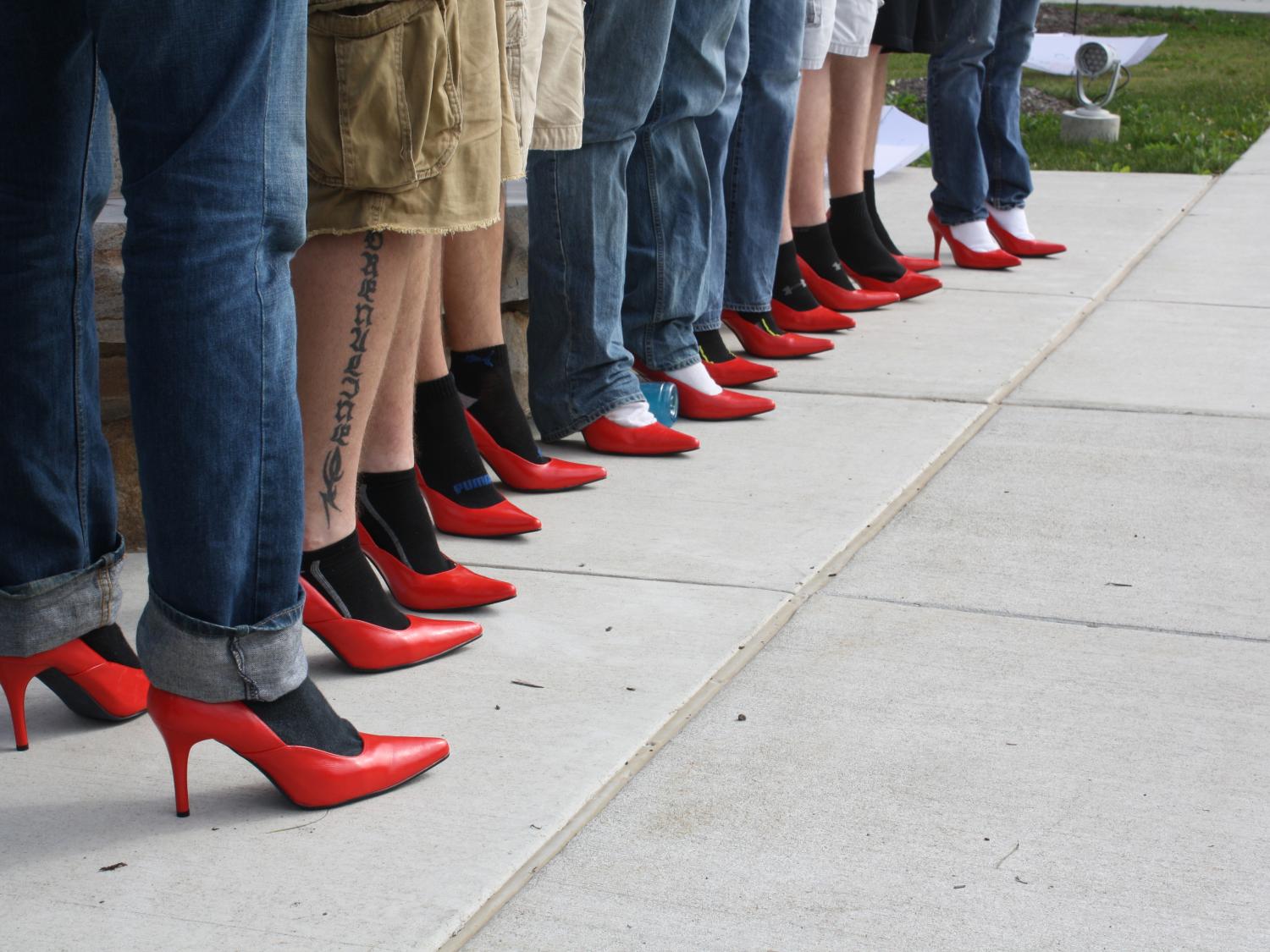 Men line up wearing red high heels. 