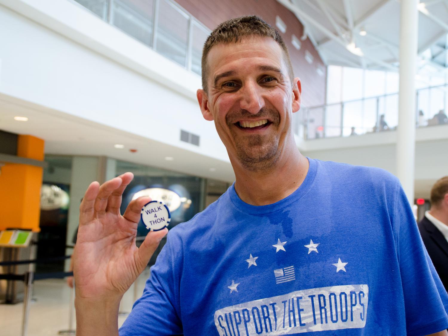 Dr. Mark Stephens wears a blue t-shirt with the words "Support the Troops," holds a small disc with the words "Walk 4 THON," and smiles.