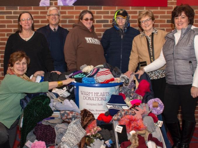 A group of men and women stand around a plastic bin filled with hats, scarves and gloves.