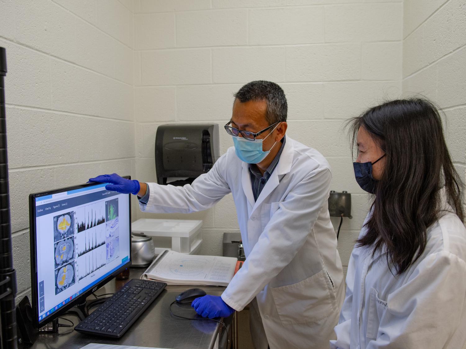 A man and a woman in lab coats look at a computer screen with brain images.