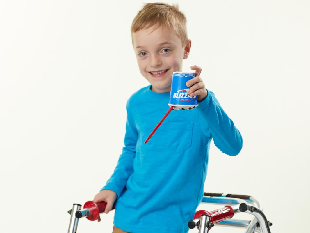 A boy smiles for a photo while holding a cup of ice cream