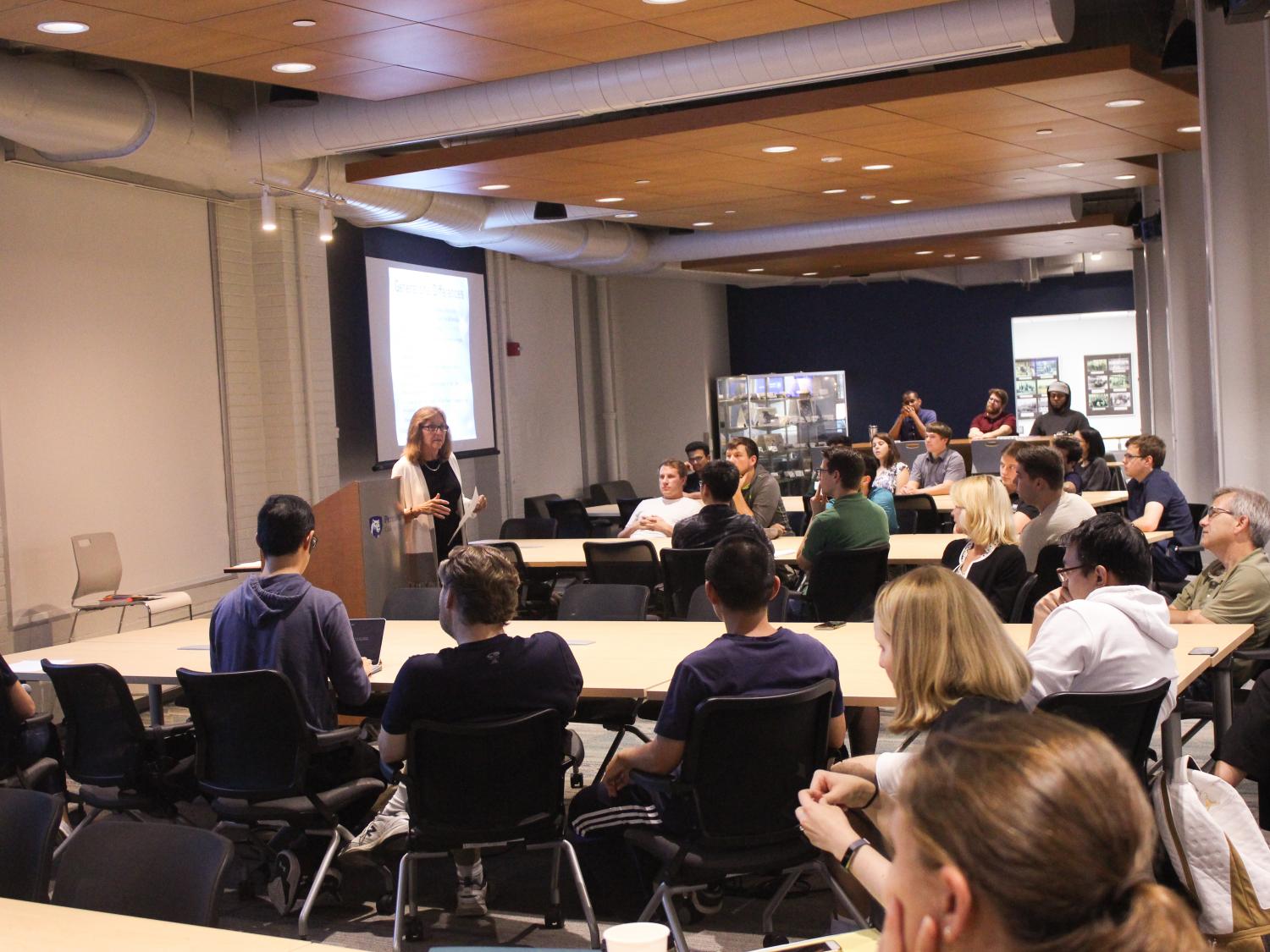 A woman delivers a lecture in front of students, faculty and staff.