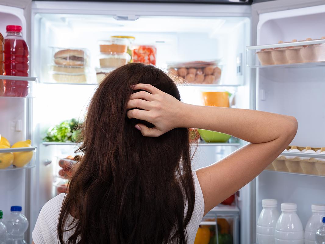 A woman looks inside an open refrigerator, deciding what to eat. 