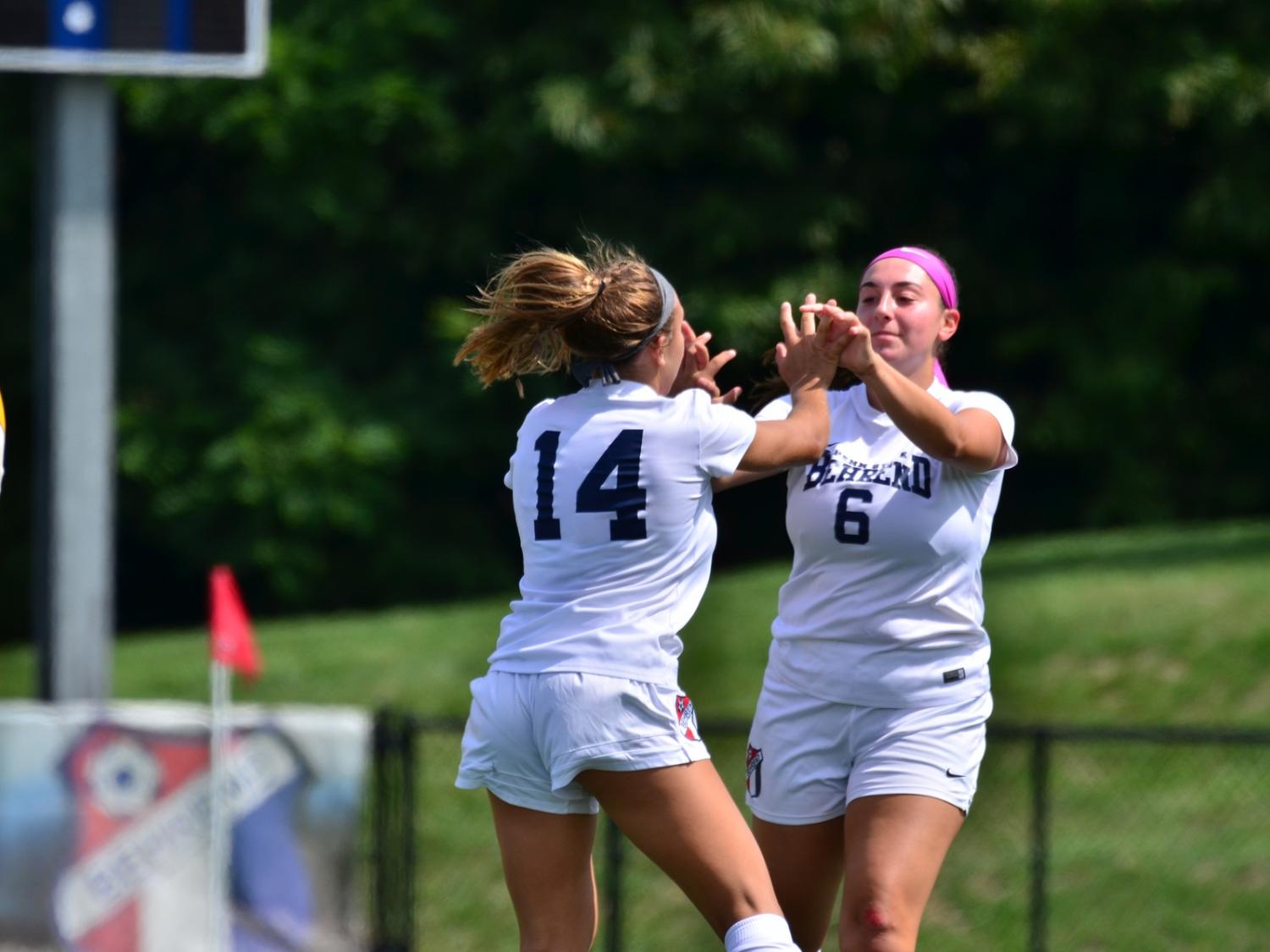 Two Penn State Behrend soccer players celebrate after scoring a goal.