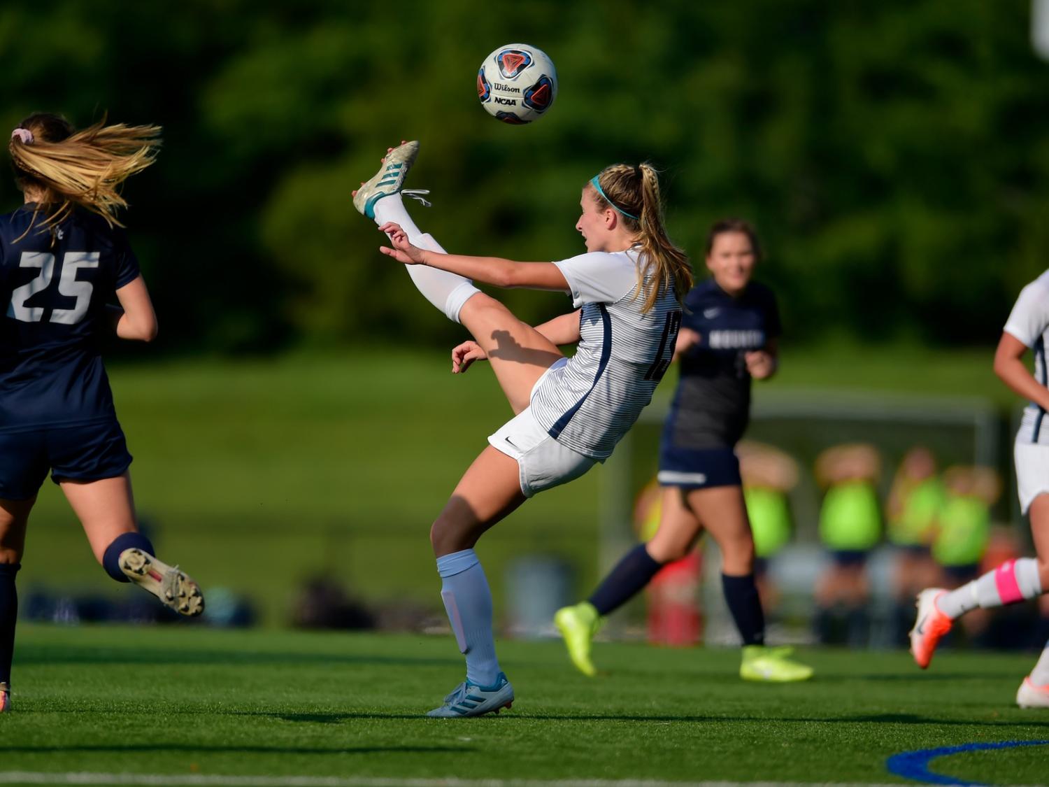 A Penn State Behrend soccer player kicks the ball above her head.