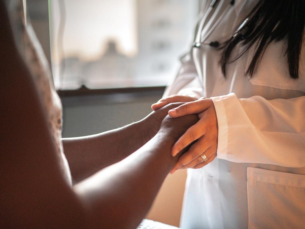 A female doctor holds the hands of her patient in a hospital room.