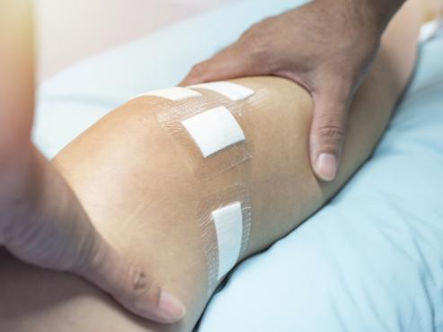A doctor's hands on a patient's leg while checking knee on exam table. 