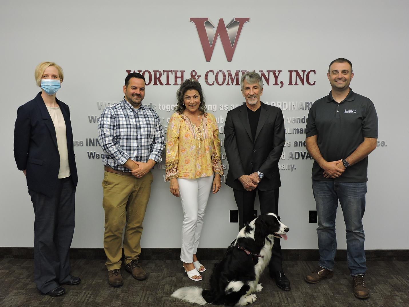 Five people from Worth and Company standing under the logo on a wall.