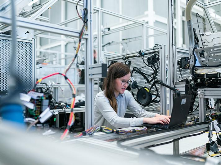 A photo of a woman working on a laptop in an industrial setting.
