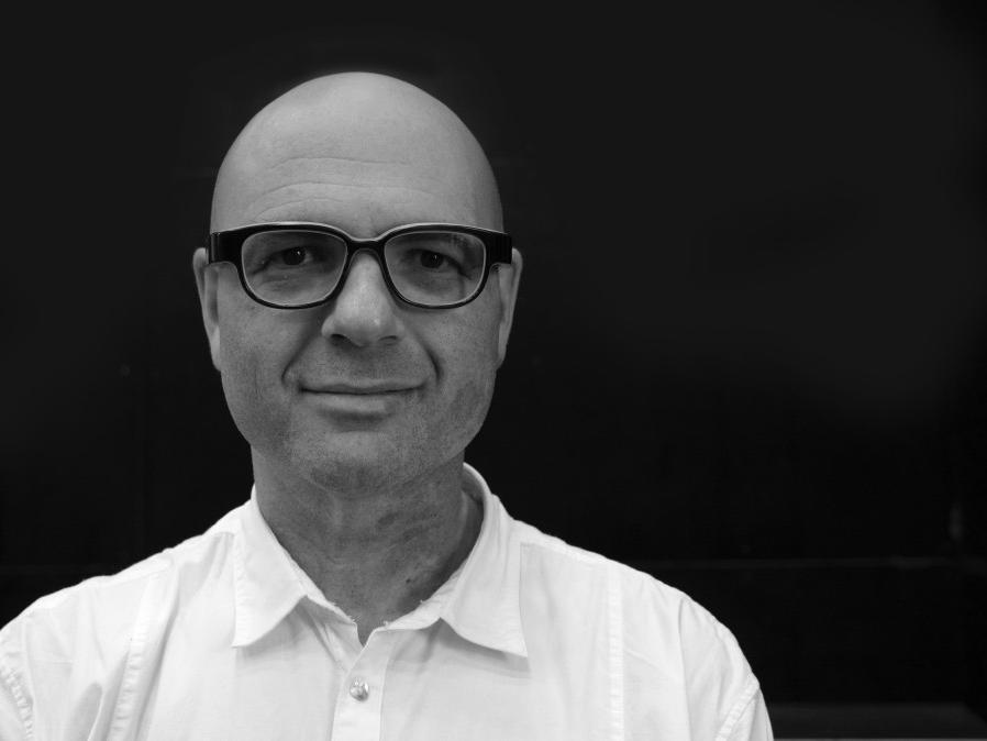 A man wearing glasses and shown from the shoulders up smiles.