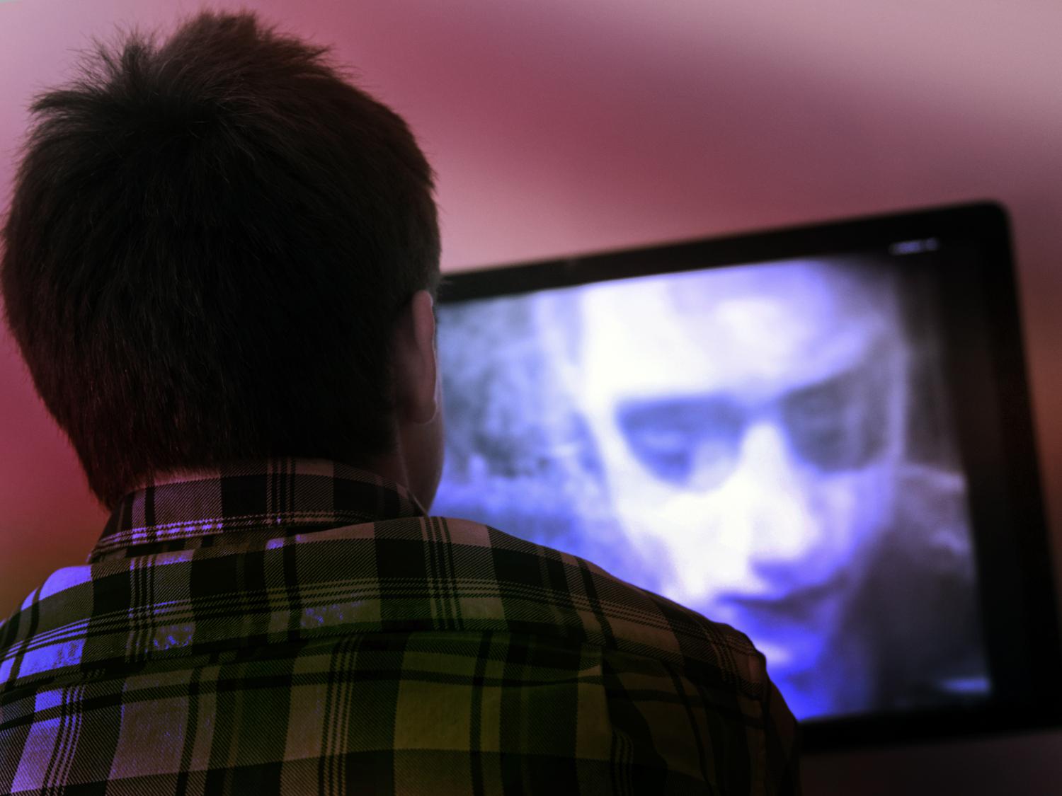 Image of the back of a viewers head while he watches a black and white zombie movie