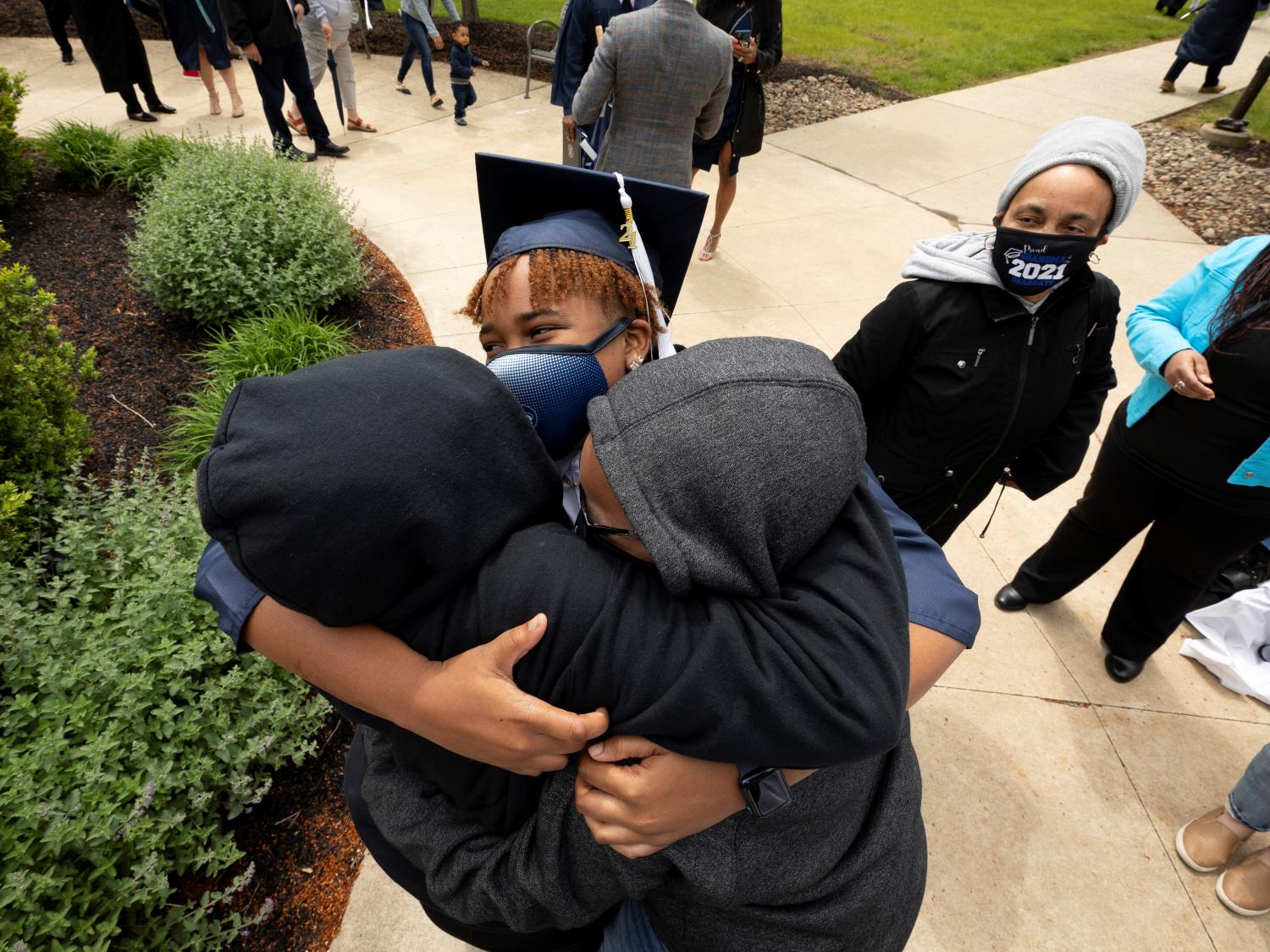 woman in mask and graduation cap hugging two people