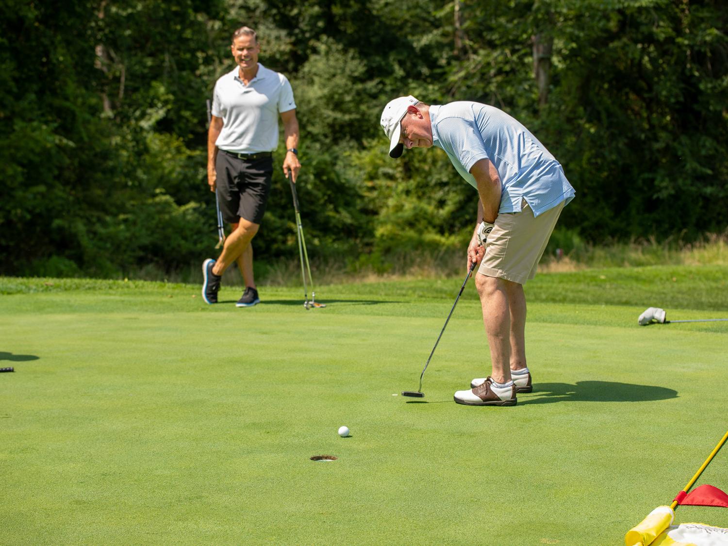A man hits a golf ball while another man watches