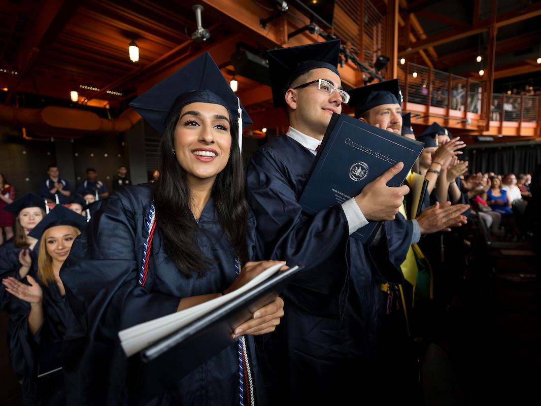 several students standing in clapping in caps and gowns