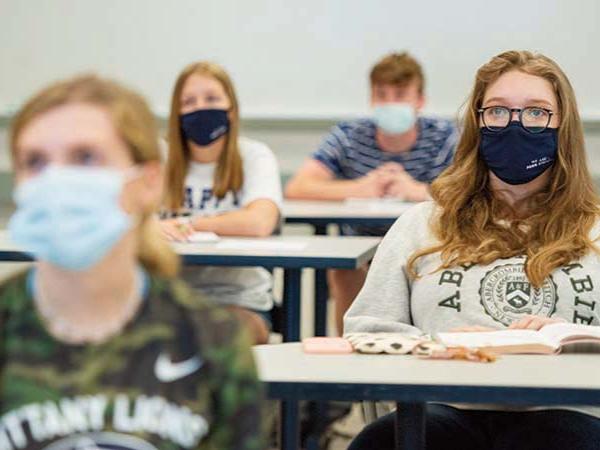 Three students wearing masks in socially distanced pattern in classroom