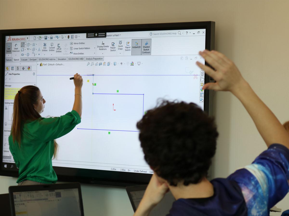 Student raising hand while professor draws on large screen television