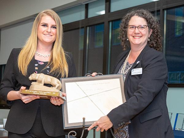 The campus chancellor stands with the award winner as they hold the plaque.