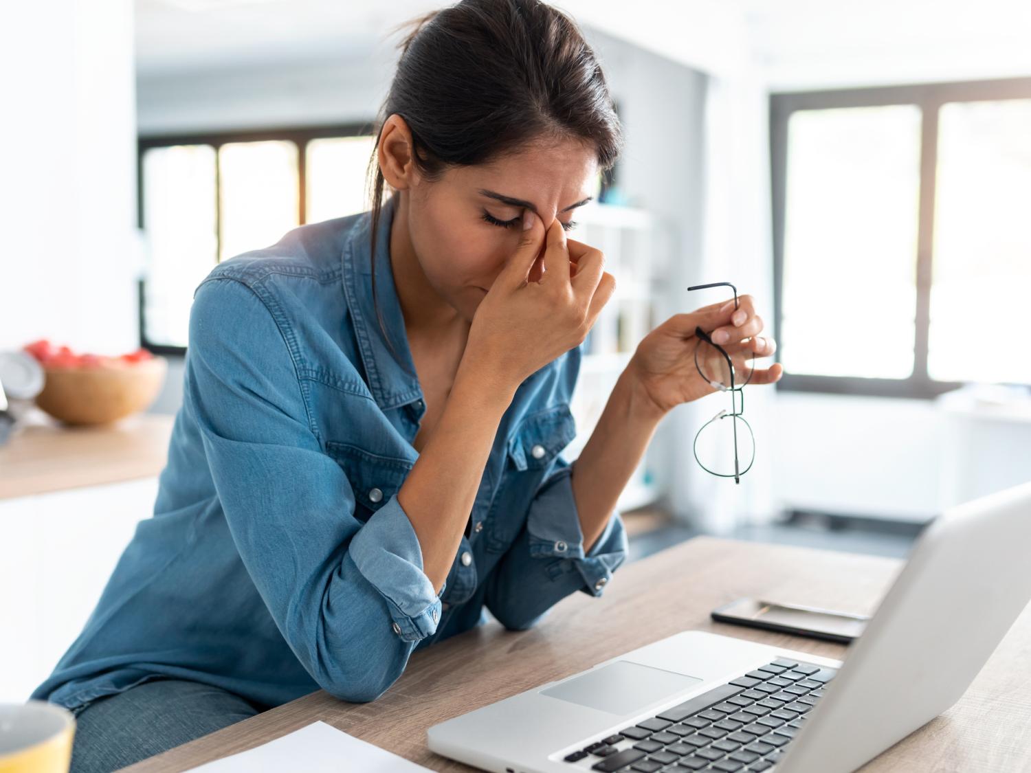 Woman sits at laptop and squeezes between her brows.