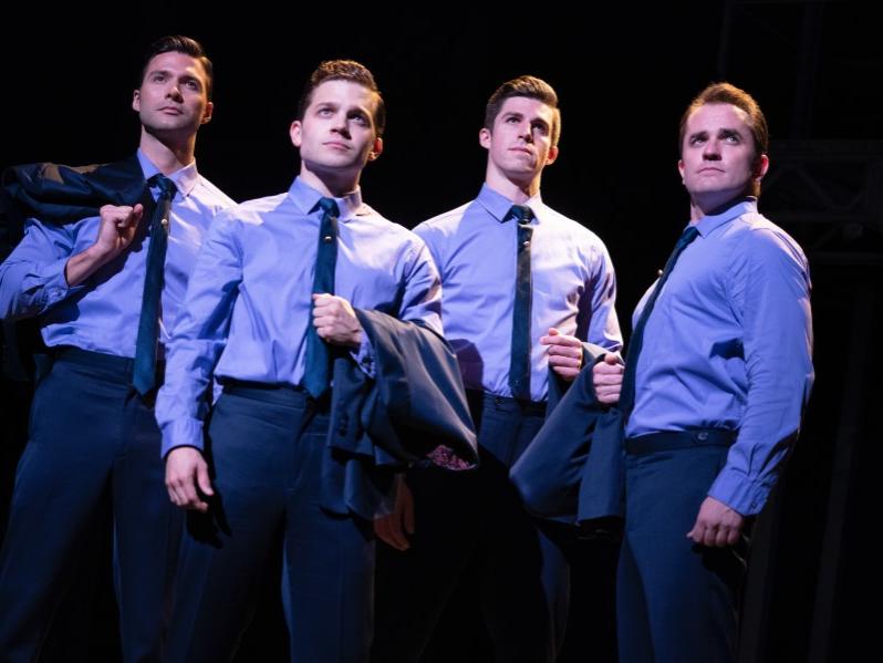 Four men dressed in identical shirts and ties stand in a line and look off into the distance.