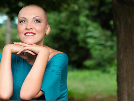A bald woman smiles while resting her head on her hands.
