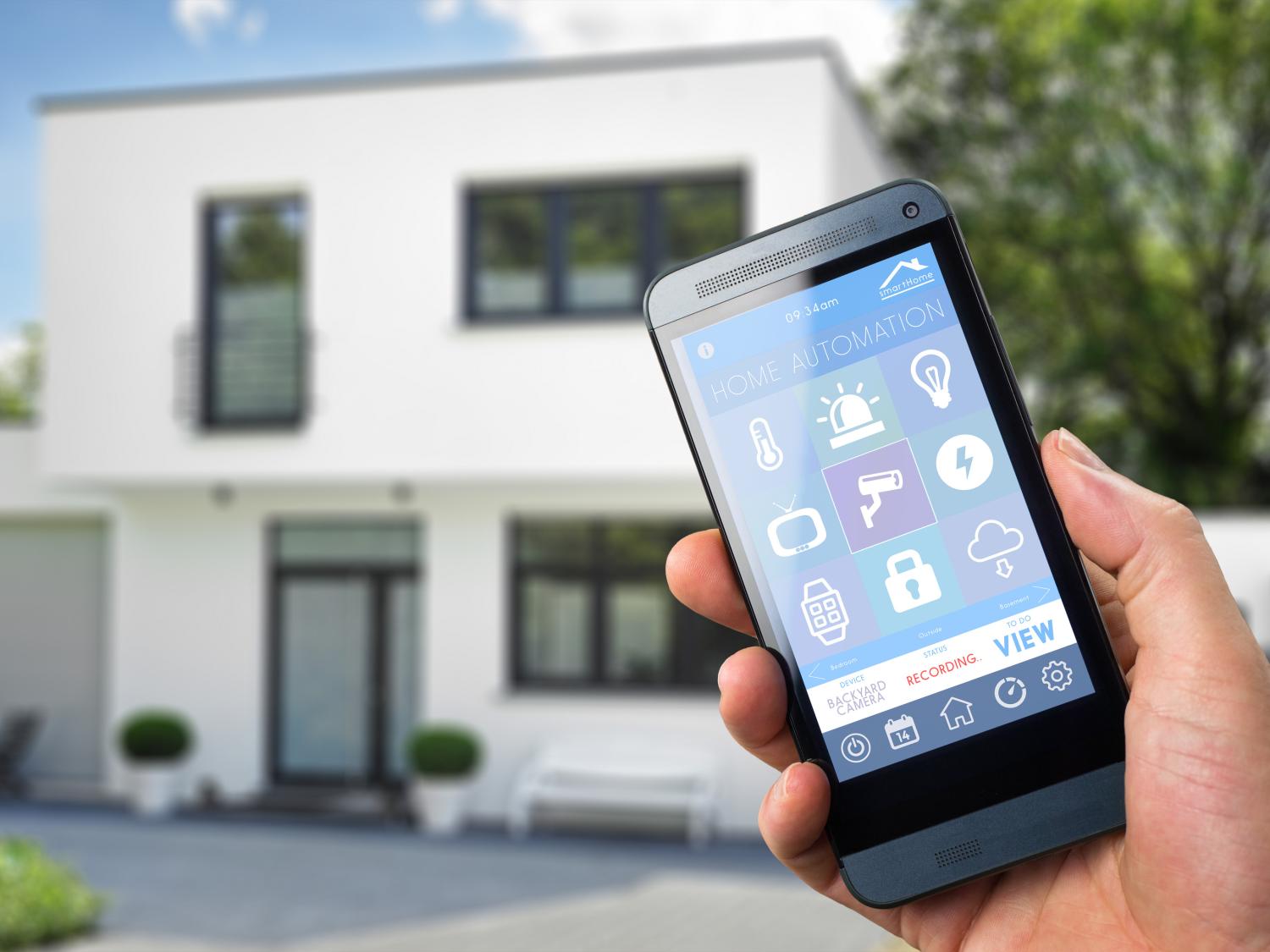 A stock photo of a man holding a smartphone in front of a house.