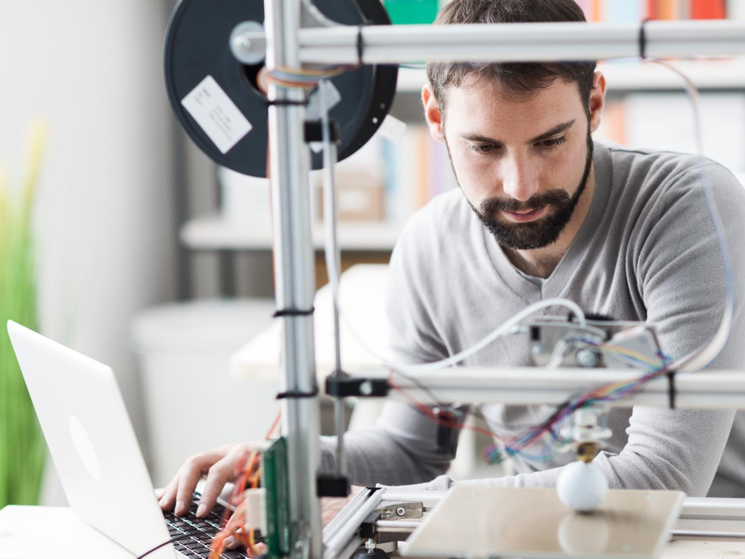 A bearded man works with a 3D printer
