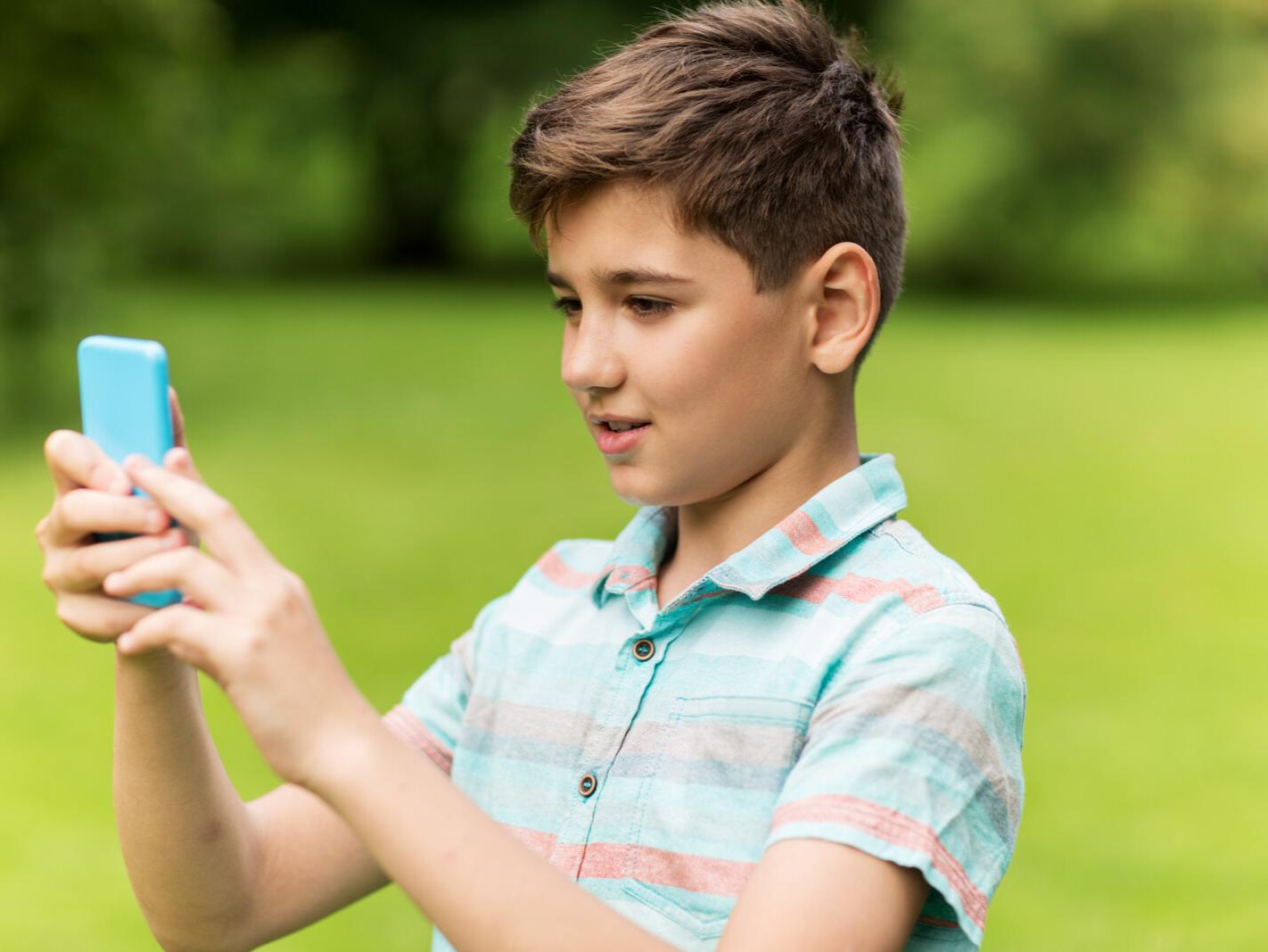 A young boy holds a smartphone while completing a virtual scavenger hunt.