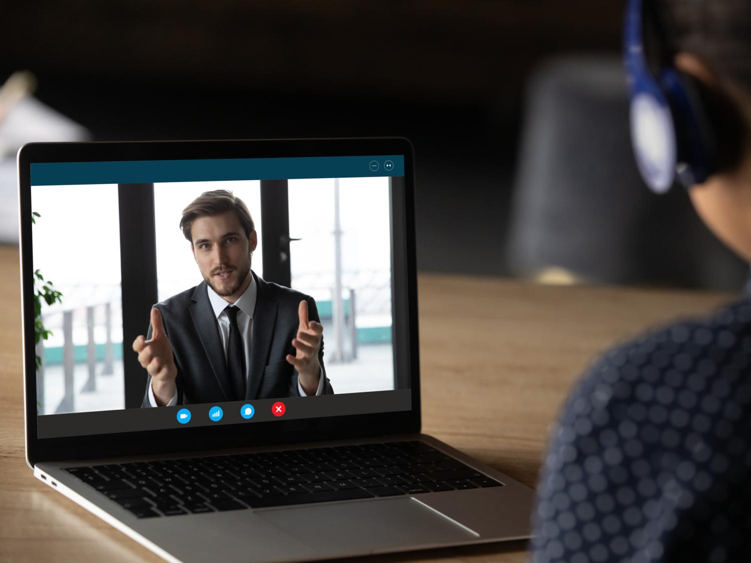 A man in a business suit talks to a woman through a computer video link.
