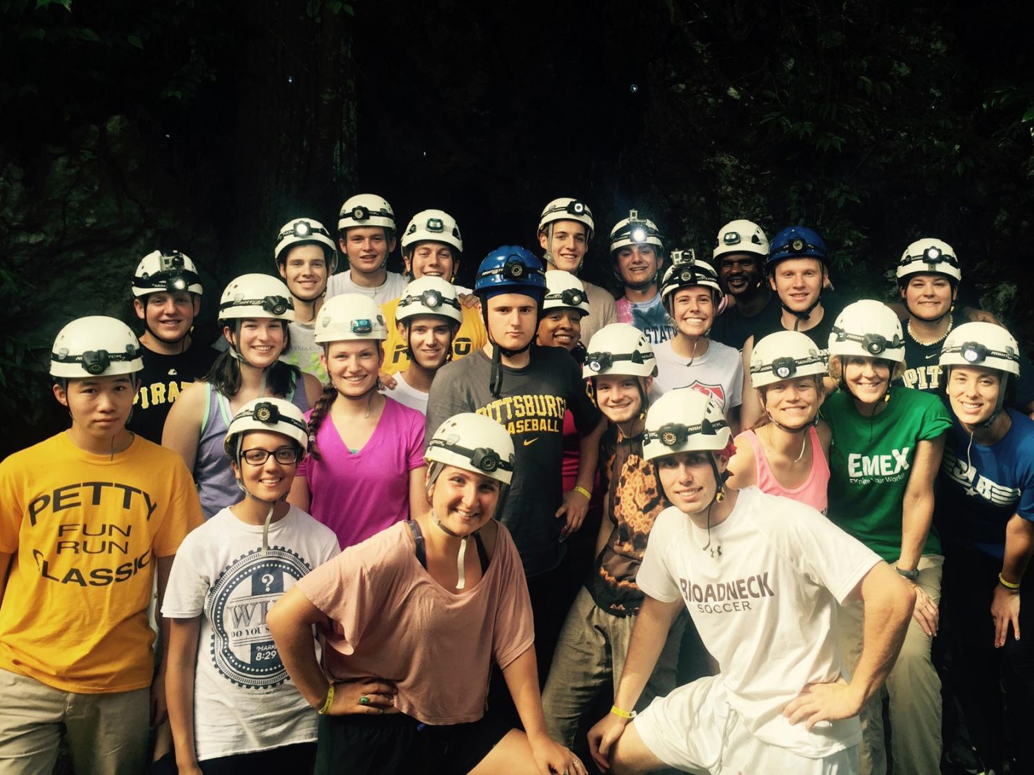 students wearing hard hats and posing in front of a cave opening