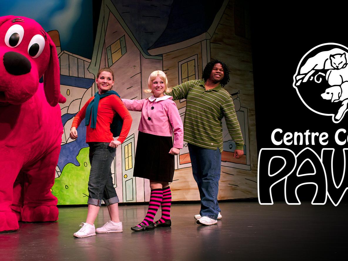 Clifford the Big Red Dog and his three companions dance on stage in front of a drawing of a neighborhood.