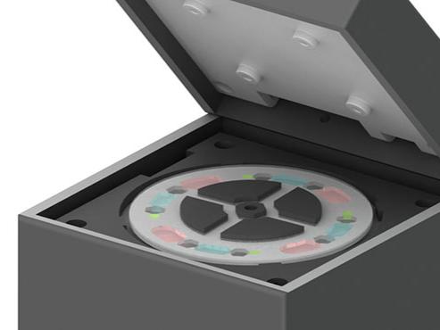 An illustration of a device that resembles a gray box with the lid lifted. On the top of the box under the lifted lid is a disk-like object. 