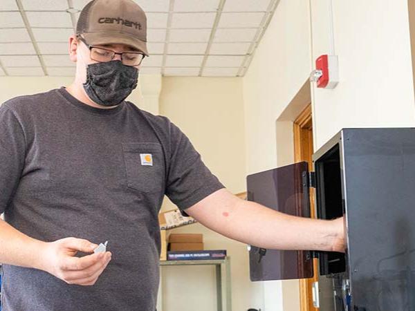 Dan Foust puts small plastic item into a 3D printer