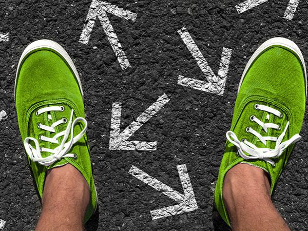 A pair of feet standing on pavement with arrows drawn in chalk pointing in multiple directions